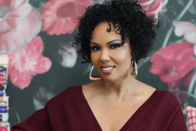 Author Jamilah Lemieux gazes at the camera with her elbow propped on the arm of a white chair. She's a Black woman with short, curly hair. She wears a dark red sweater.