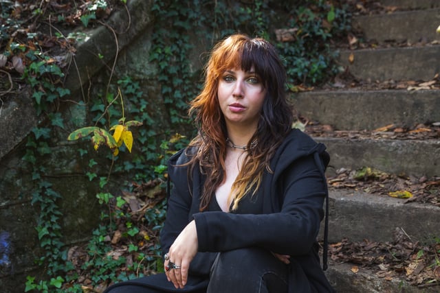 Hillary Gonzalez dressed in all black, sitting on outdoor steps.