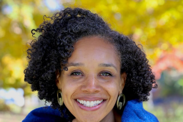 Author Christena Cleveland smiles brightly at the camera. She's a Black woman with short curly hair. She wears a bright blue top..